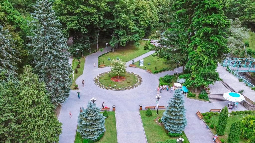 Вид с воздуха на Центральный парк Боржоми: круглая клумба, голубые ели, скамейки и прогуливающиеся посетители