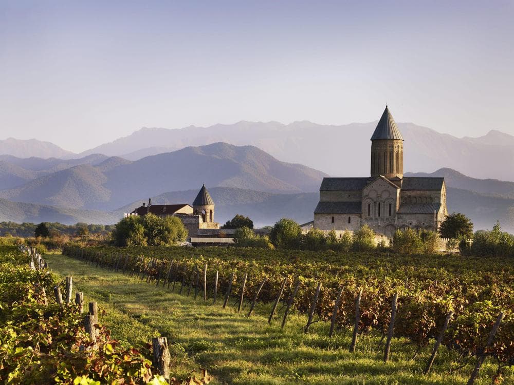 Alaverdi Monastery rising above autumn vineyards in Kakheti, with misty Caucasus mountains behind
